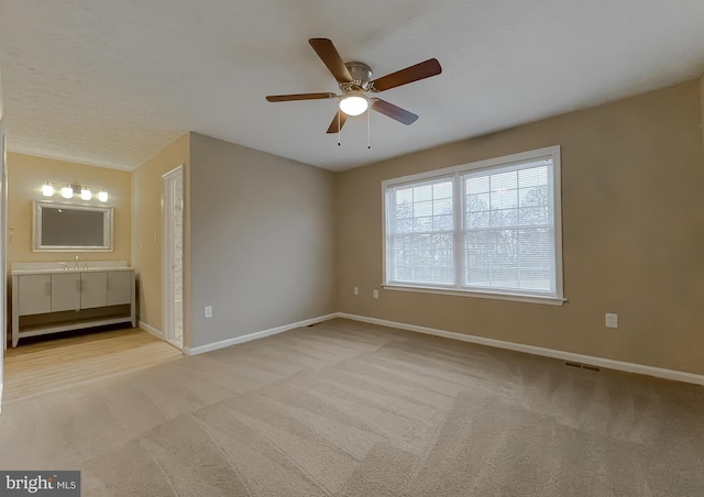 unfurnished bedroom with ceiling fan, sink, light carpet, and ensuite bath