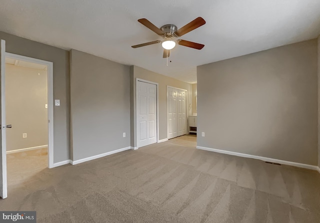 unfurnished bedroom featuring ceiling fan, light colored carpet, and multiple closets