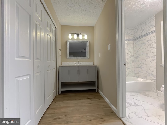 full bathroom with hardwood / wood-style floors, tiled shower / bath combo, vanity, toilet, and a textured ceiling