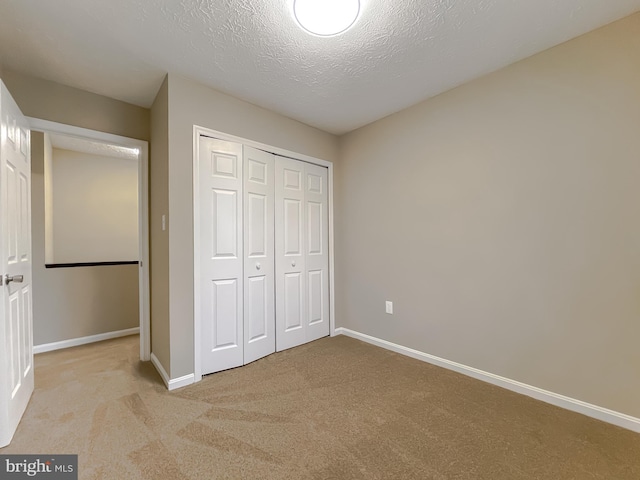 unfurnished bedroom featuring light colored carpet, a closet, and a textured ceiling