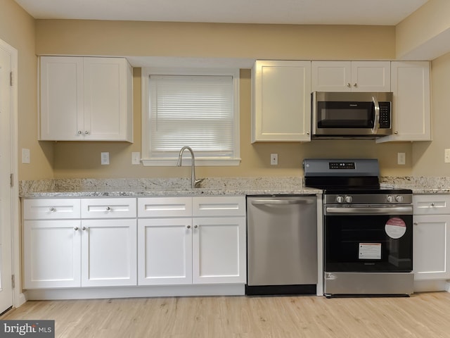 kitchen with sink, white cabinetry, light stone counters, appliances with stainless steel finishes, and light hardwood / wood-style floors