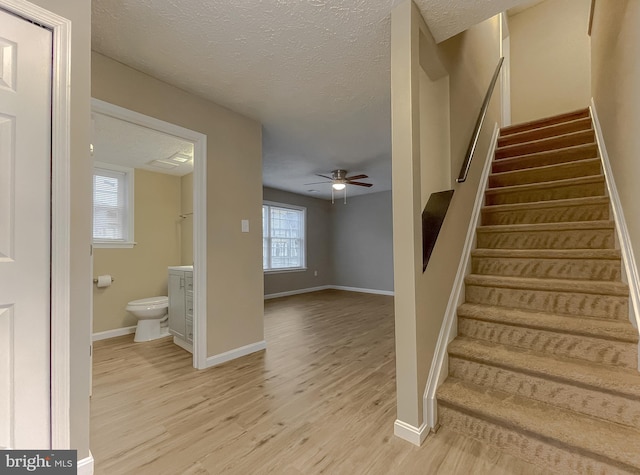 stairs with ceiling fan, hardwood / wood-style flooring, and a textured ceiling