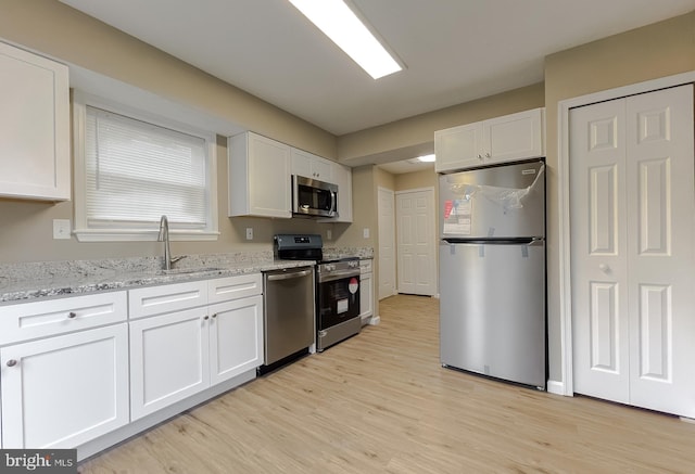 kitchen with sink, white cabinets, light stone counters, light hardwood / wood-style floors, and stainless steel appliances