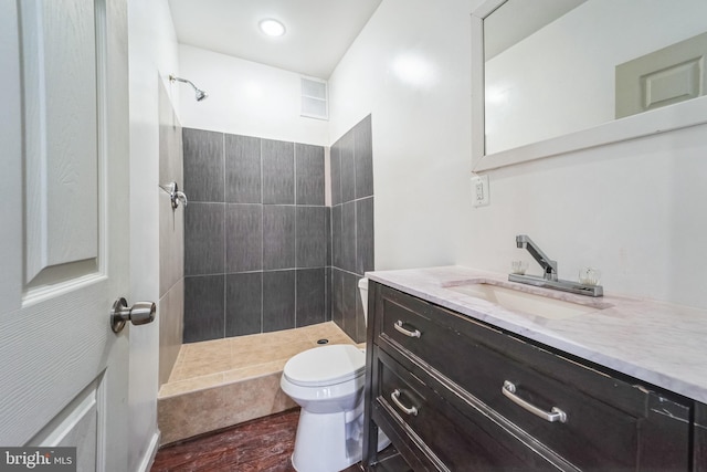 bathroom featuring vanity, hardwood / wood-style flooring, toilet, and tiled shower