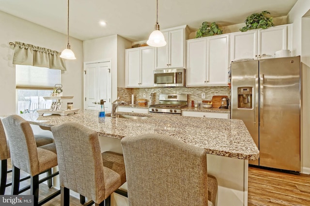 kitchen featuring appliances with stainless steel finishes, tasteful backsplash, white cabinetry, hanging light fixtures, and a kitchen island with sink