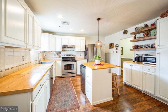 kitchen with appliances with stainless steel finishes, pendant lighting, wood counters, white cabinets, and a center island