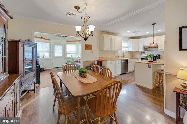 dining area with sink, crown molding, light hardwood / wood-style flooring, and ceiling fan with notable chandelier