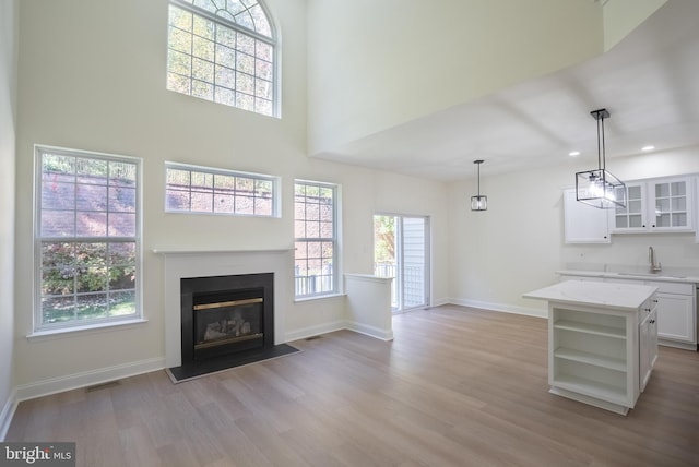 unfurnished living room featuring a towering ceiling, sink, and light wood-type flooring