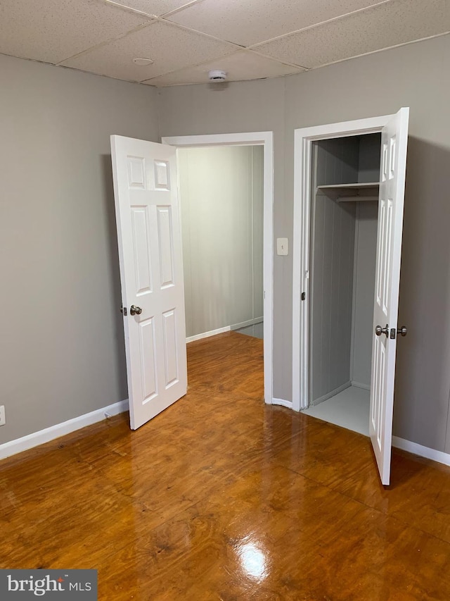 unfurnished bedroom with a paneled ceiling, hardwood / wood-style floors, and a closet