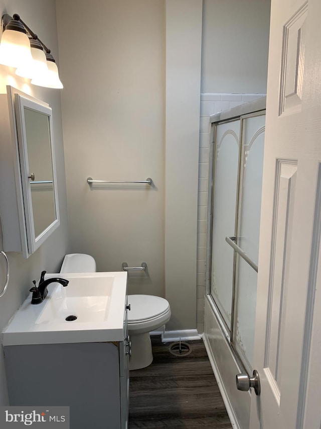 full bathroom featuring vanity, hardwood / wood-style floors, enclosed tub / shower combo, and toilet