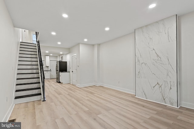 basement with stainless steel refrigerator and light hardwood / wood-style floors