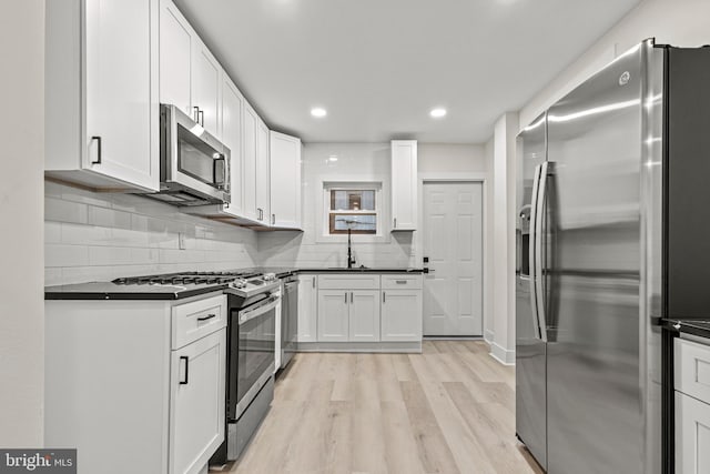 kitchen featuring sink, light hardwood / wood-style flooring, appliances with stainless steel finishes, white cabinets, and backsplash