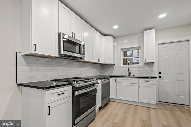 kitchen with appliances with stainless steel finishes, sink, backsplash, white cabinets, and light wood-type flooring