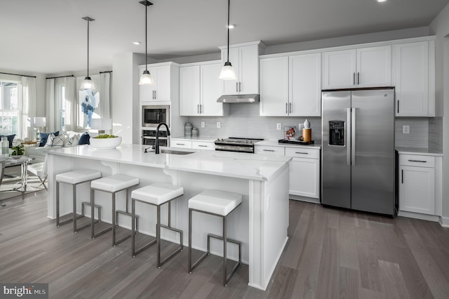 kitchen with backsplash, under cabinet range hood, a breakfast bar area, appliances with stainless steel finishes, and a sink