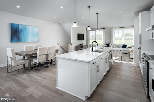 kitchen with a sink, light stone countertops, light wood-type flooring, white cabinetry, and a kitchen island with sink