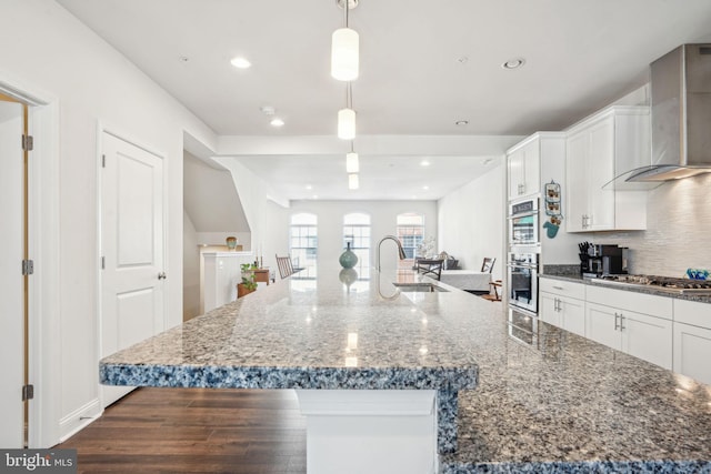 kitchen with stainless steel gas cooktop, white cabinetry, wall chimney range hood, and a sink