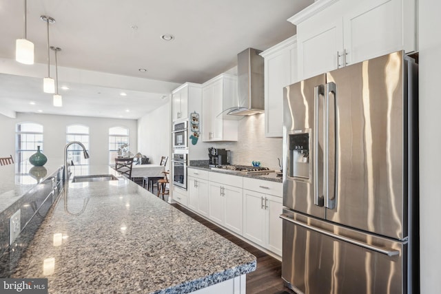 kitchen featuring a sink, tasteful backsplash, appliances with stainless steel finishes, wall chimney exhaust hood, and white cabinets