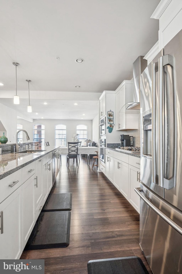 kitchen with light stone counters, dark wood-style floors, appliances with stainless steel finishes, wall chimney exhaust hood, and white cabinets