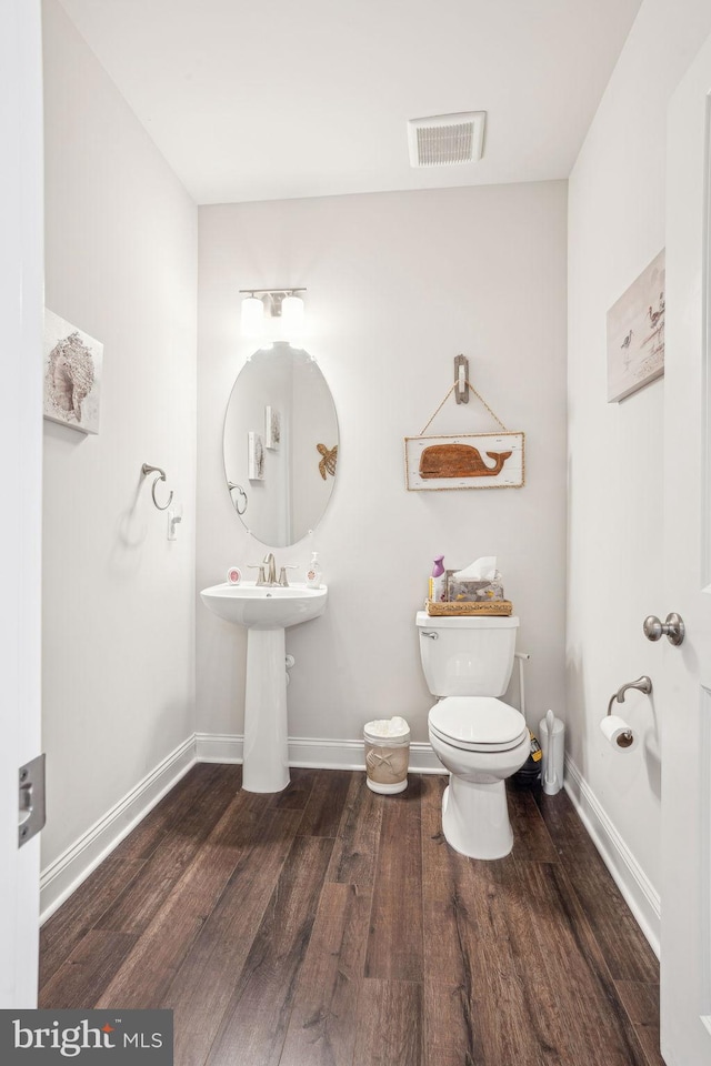 half bathroom with visible vents, baseboards, toilet, and wood finished floors