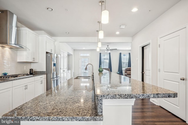 kitchen with a sink, backsplash, stainless steel appliances, wall chimney exhaust hood, and white cabinets