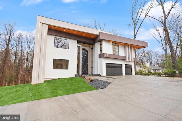 modern home featuring a garage, a front lawn, concrete driveway, and stucco siding