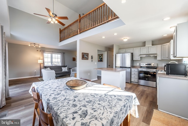 dining space featuring a towering ceiling, dark wood-type flooring, and ceiling fan