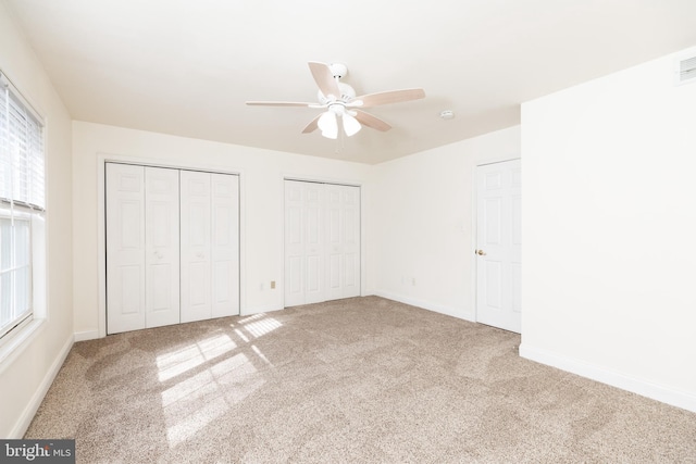 unfurnished bedroom featuring ceiling fan, carpet, and two closets