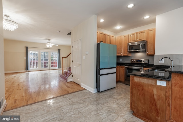 kitchen featuring sink, dark stone countertops, appliances with stainless steel finishes, ceiling fan with notable chandelier, and decorative backsplash