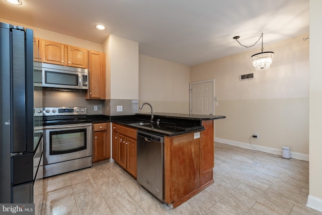 kitchen with sink, appliances with stainless steel finishes, decorative light fixtures, kitchen peninsula, and dark stone counters