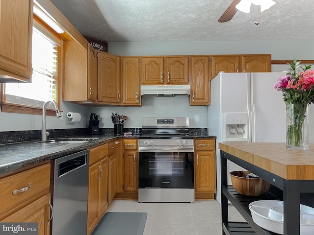 kitchen with brown cabinets, appliances with stainless steel finishes, a sink, a textured ceiling, and under cabinet range hood