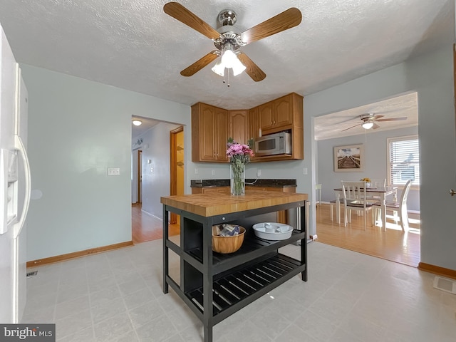 kitchen featuring visible vents, brown cabinetry, butcher block countertops, stainless steel microwave, and light floors