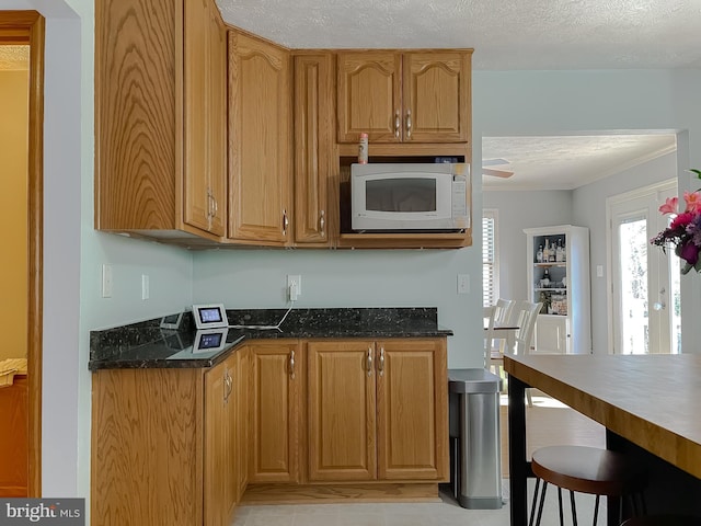 kitchen featuring dark stone counters, brown cabinets, a textured ceiling, and white microwave