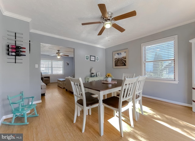 dining space featuring baseboards, crown molding, a textured ceiling, and light wood finished floors