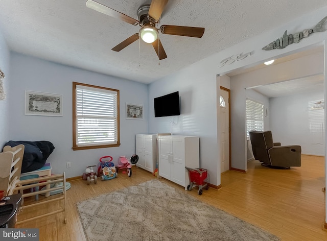 rec room with a textured ceiling, light wood-type flooring, and baseboards