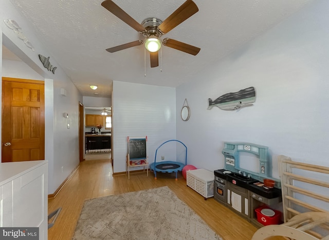 playroom with a textured ceiling, light wood-type flooring, and baseboards