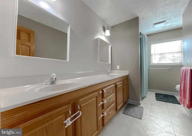 bathroom with a textured ceiling, double vanity, tile patterned flooring, and a sink