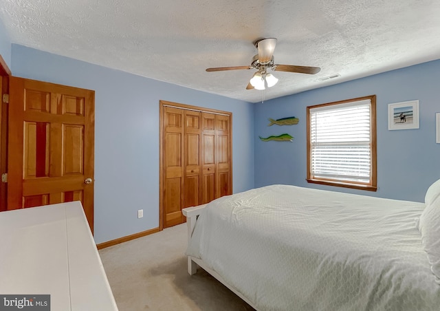 bedroom with a closet, visible vents, light carpet, a textured ceiling, and baseboards