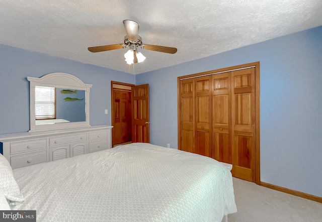 bedroom featuring a textured ceiling, ceiling fan, light colored carpet, baseboards, and a closet