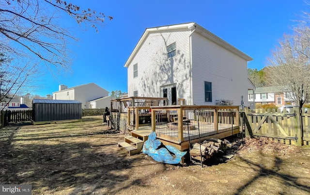 back of property with fence, a deck, and a shed