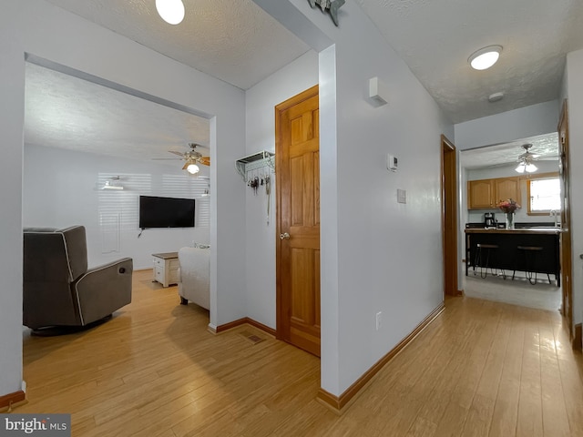 hallway with light wood-style flooring, baseboards, and a textured ceiling