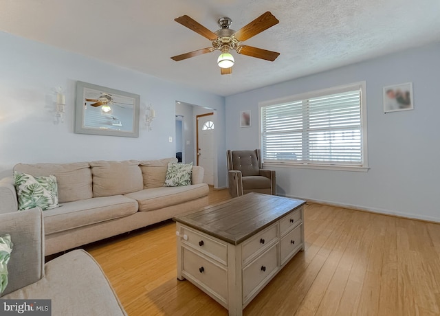 living area with a ceiling fan, light wood-type flooring, a textured ceiling, and baseboards