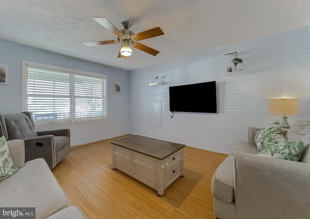 living room with baseboards, ceiling fan, a textured ceiling, and light wood finished floors