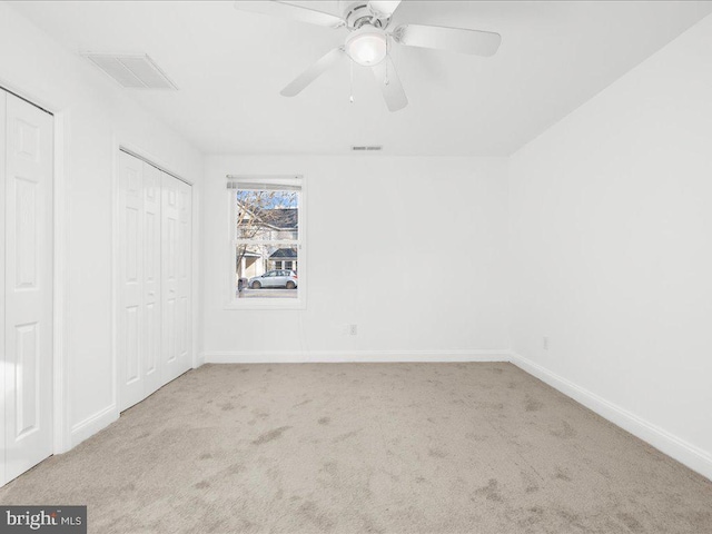 unfurnished bedroom featuring light carpet, multiple closets, and ceiling fan