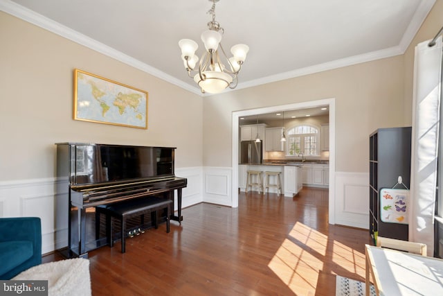 sitting room featuring dark wood finished floors, ornamental molding, a wainscoted wall, and a chandelier