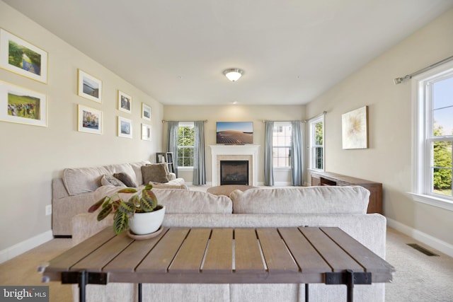 carpeted living room with a fireplace, a healthy amount of sunlight, visible vents, and baseboards