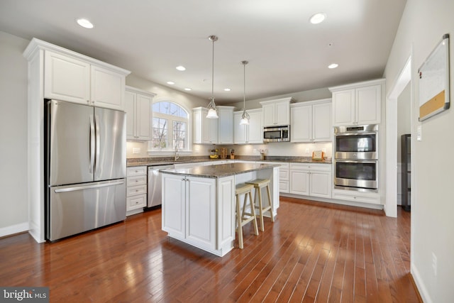 kitchen featuring dark wood finished floors, a center island, white cabinetry, stainless steel appliances, and a breakfast bar area