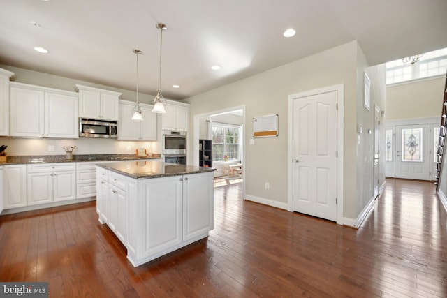 kitchen with white cabinetry, appliances with stainless steel finishes, a kitchen island, and dark wood-type flooring