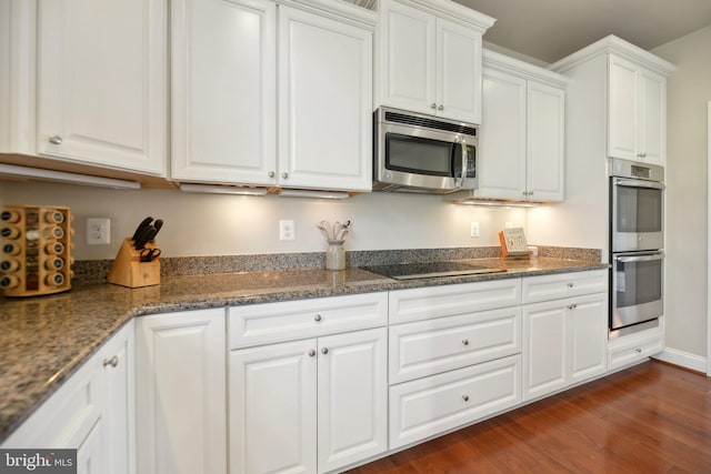 kitchen with dark stone countertops, appliances with stainless steel finishes, white cabinetry, and dark wood-style flooring