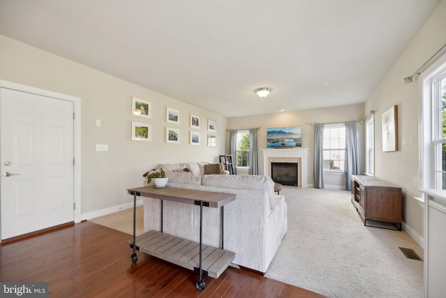 living area featuring visible vents, baseboards, wood finished floors, and a fireplace with flush hearth