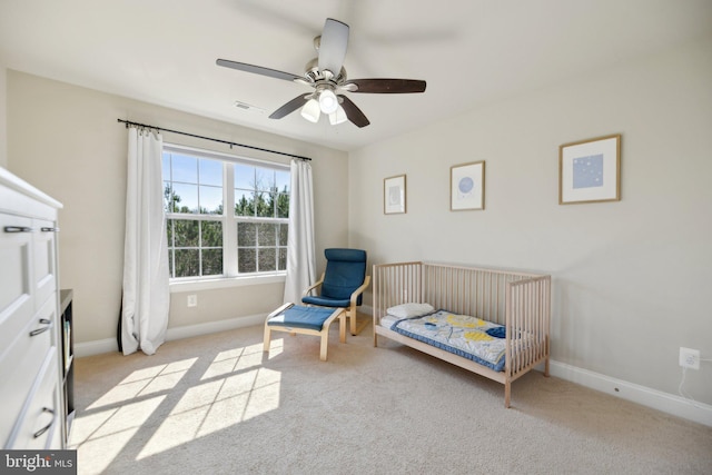 bedroom featuring visible vents, a nursery area, baseboards, light colored carpet, and ceiling fan